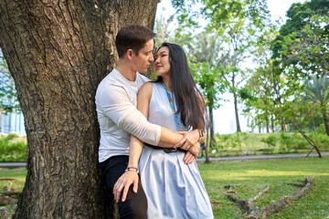 Fototapeta premium Multiracial couple about to kiss leaning against a tree