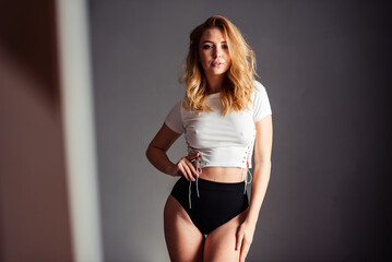 A slender blonde with her hair tossed to one side looks sexy at the camera in a white top and high shorts
