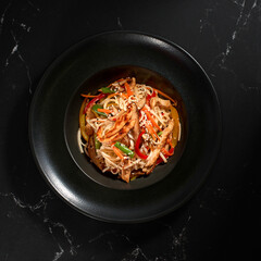 Pasta. udon noodles with Chicken and vegetables on a plate on black stone background.
