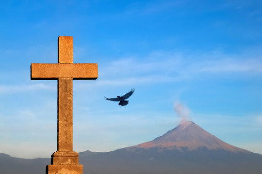 Christian cross and raven on the background of the active volcano Popokatepetl. Catholic Church of St. Mary. Mexico. Cholula city.