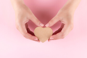 Female hands with beautiful natural manicure - pink nude nails with cardboard heart on pink background