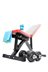 Dumbbells beneath a workout bench with towel and water bottle