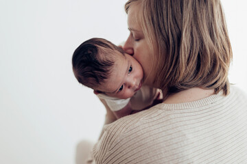 back view of a mum kissing her biracial newborn baby child against white background.