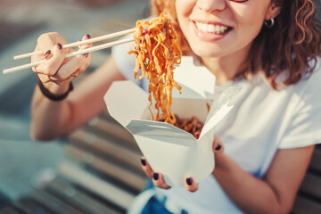 Young woman having a lunch break and eating wok noodles outdoors. Fastfood meal concept