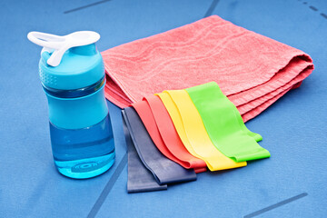 Resistance rubber bands, towel and water bottle on blue mat