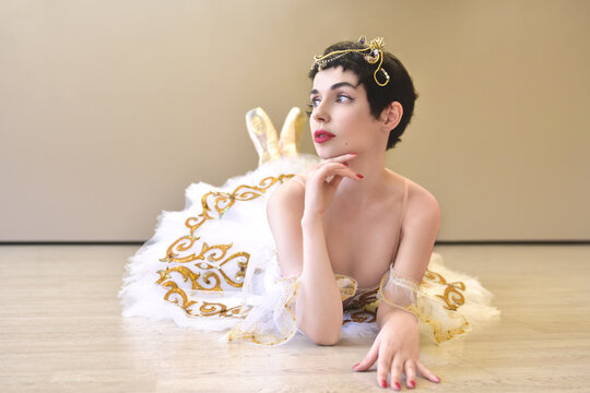 A portrait of a ballerina lying on the floor in a ballroom, she touches her chin with her hand and looks flirtatiously