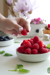 A bowl with fresh raspberries and a female hand takes a berry close up