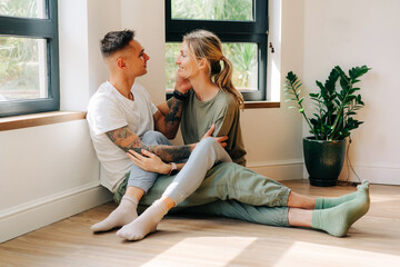 Young happy couple in their new apartment hugging while sitting on the floor on a date.