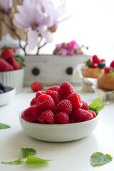 A bowl with fresh raspberries in the background kitchen decor, magnolia and fresh berries close up