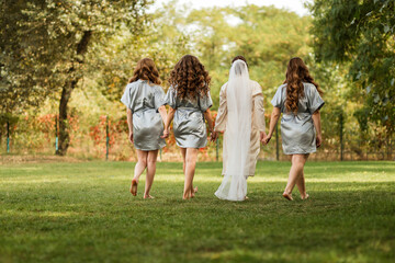 Naklejka na ściany i meble bridesmaids and bride walk on the lawn, morning of the bride