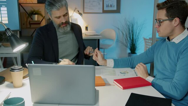 Ambitious business men and women conversing working in modern office in the evening. Entrepreneurs and professional cooperation concept.