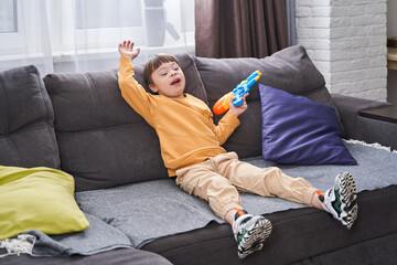 Joyful male kid with down syndrome sitting at the sofa and playing