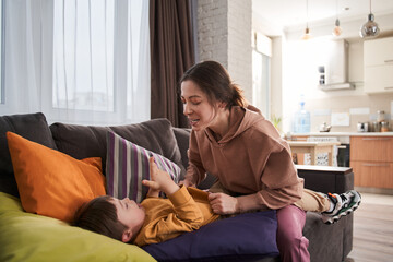 Mother and her son with Down syndrome playing at the sofa at the living room
