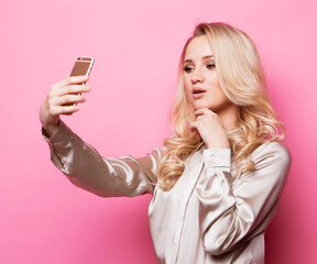 Naklejka premium woman in casual clothes with perfect makeup and hair style with smartphone, makes selfie over pink background.