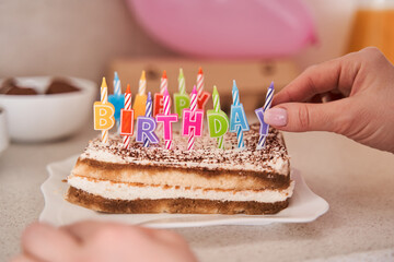 Female putting candles at the birthday cake while preparing to the anniversary party