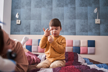Boy with Down syndrome sitting at the bed and talking with his mother