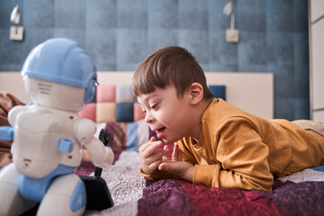 Boy with Down syndrome laying at the bed with his toy while relaxing