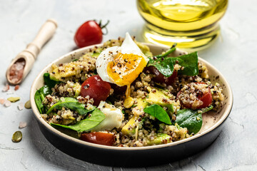 Keto diet plate quinoa, avocado, egg, tomatoes, spinach and sunflower seeds on light background....