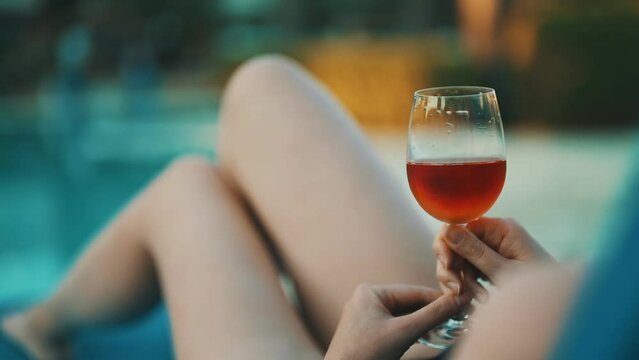Woman with glass of wine is relaxing by the pool.