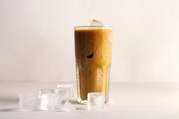 Cold coffee with cream and ice. Glass with coffee in drops of water and melting ice on the table