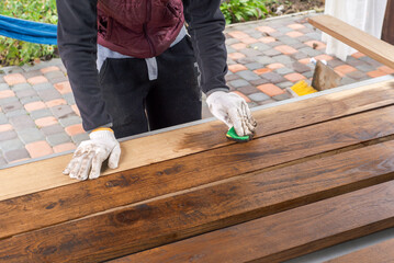 Brown color stain painting on wooden table or fence or wall, or flour, use for home decorated. House renovation. Half - painted surface. Hand holding brush. Background with copy space.