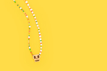 The chain with a skull pendant is made of multicolored beads and pearls on a yellow background.