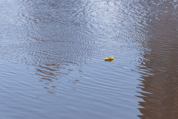 A small yellow lonely boat is floating in the water. A toy