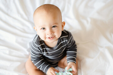 little boy 6 months old sits on a white blanket and smiles