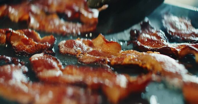 Closeup slider shot of fresh bacon being flipped on a griddle. 4K cinematic footage.