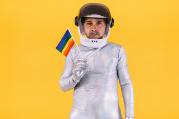 Gay man dressed as an astronaut with a helmet and silver suit with a rainbow lgtbi collective flag,...