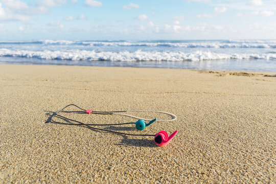 Ear plugs with cord for surfing on sandy beach against ocean waves.
