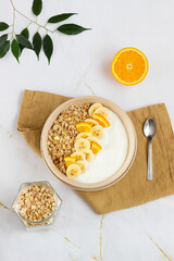 Bowl with muesli, yogurt and fruit on white marble table