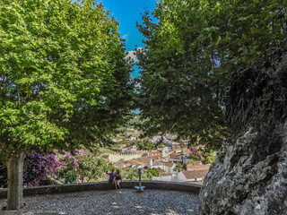 Obidos, Portugal. View of the town, the medieval walls, and historic houses, trough two lush trees. Two tourists taking photographies