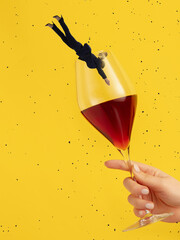 Contemporary art collage. Woman in a suit diving into wine glass isolated over yellow background