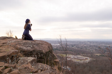 Woman kneeling and looking up in prayer at mountain overlook