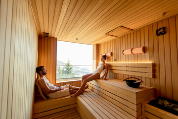 Young couple relaxing in the sauna and watching winter forest through the window