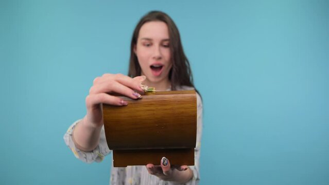 Cute positina woman tore off a wooden box with a smile on her face on a blue background, she is in a drunken shock from what she saw