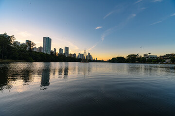 Igapo lake at sunset, Londrina - PR, Brazil. Beautiful city lake surrounded by trees, with calm water and the city buildings on background.