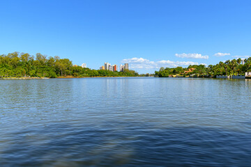 Wide view of Igapo lake, Londrina - PR, Brazil. Beautiful city lake, with trees around the shore and the city buildings on background, on a blue sky day.