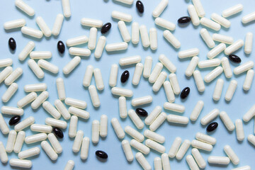 Many white pills and black capsules on blue background