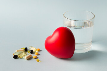 Health composition with red heart, glass of water and vitamin pills, capsules on blue background