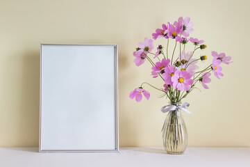 Large silver A4 mockup blank frame with pink summer flowers in glass vase on yellow wall background