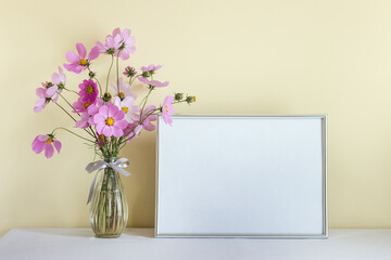 Large silver horizontal A4 mockup blank frame with pink summer flowers in glass vase on yellow wall background
