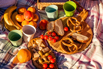 Top view of healthy picnic food on wooden board on blanket outdoors at sunny summer day. Sunset time, light and shadows.Fruit, cheese, tomatoes and freshbaked homemade bread.