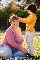 cute little boy having fun with his grandmother playing with her hair in spring blooming garden outdoors at sunny day