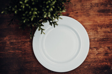 white empty plate on a wooden table with green plant