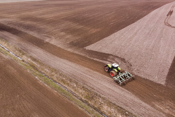 A tractor with a disc harrow plows a field for sowing. Aerial photography.