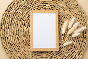 Top view photo of wooden photo frame and branch of white lagurus flowers on decorative serving mat with copyspace