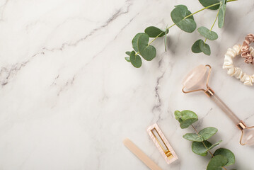 Skincare beauty procedure concept. Top view photo of pink barrette nail file rose quartz roller scrunchies and eucalyptus on white marble background with copyspace
