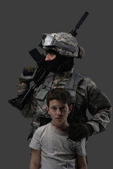 Shot of brave soldier with rifle protecting little child isolated on gray background.